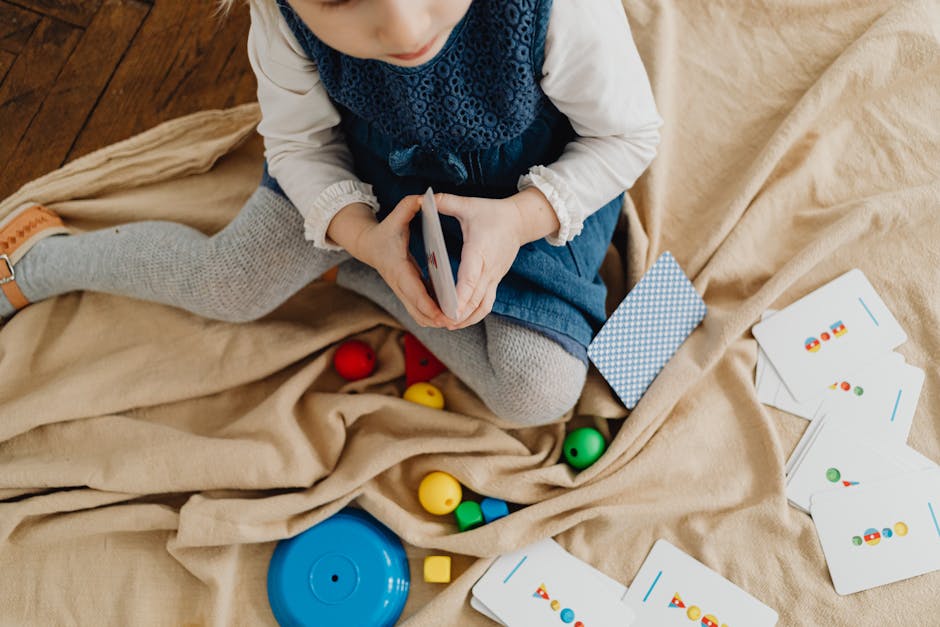 A young girl engaged with colorful educational flash cards and toys on a mat indoors.