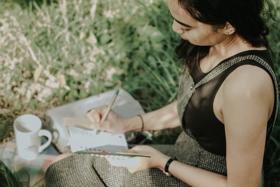 Young woman journaling outdoors, enjoying a peaceful moment with nature, pen in hand.