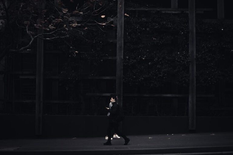 A solitary figure walks along a dimly lit urban street, capturing a moody city atmosphere.