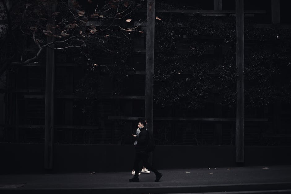 A solitary figure walks along a dimly lit urban street, capturing a moody city atmosphere.