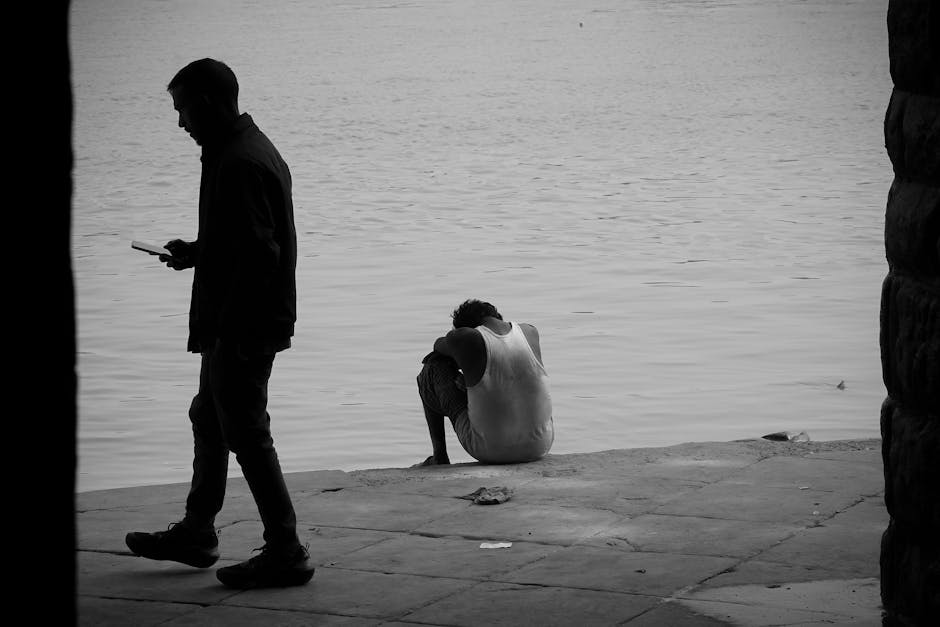 Black and white photo of a person sitting by the river in deep thought.