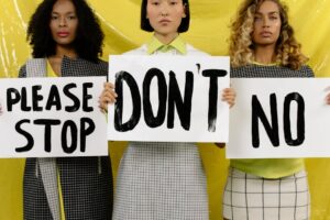 Three diverse women holding protest signs against yellow background promoting unity and activism.