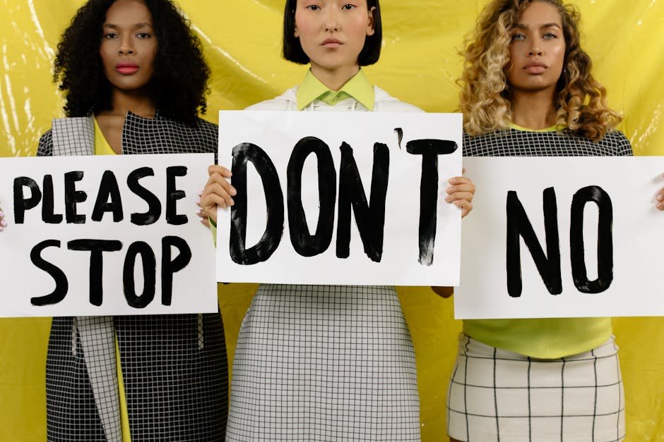 Three diverse women holding protest signs against yellow background promoting unity and activism.