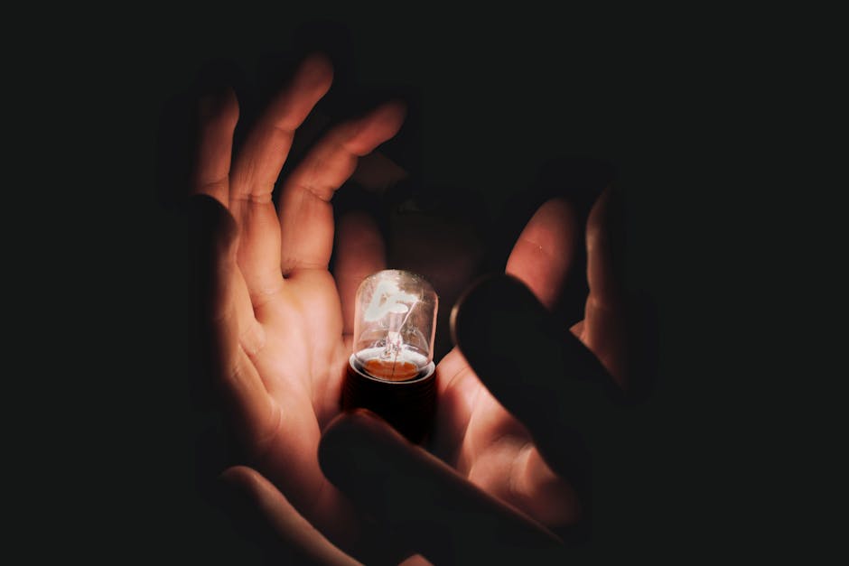 Closeup of anonymous person demonstrating burning lightbulb in palms in middle of darkness