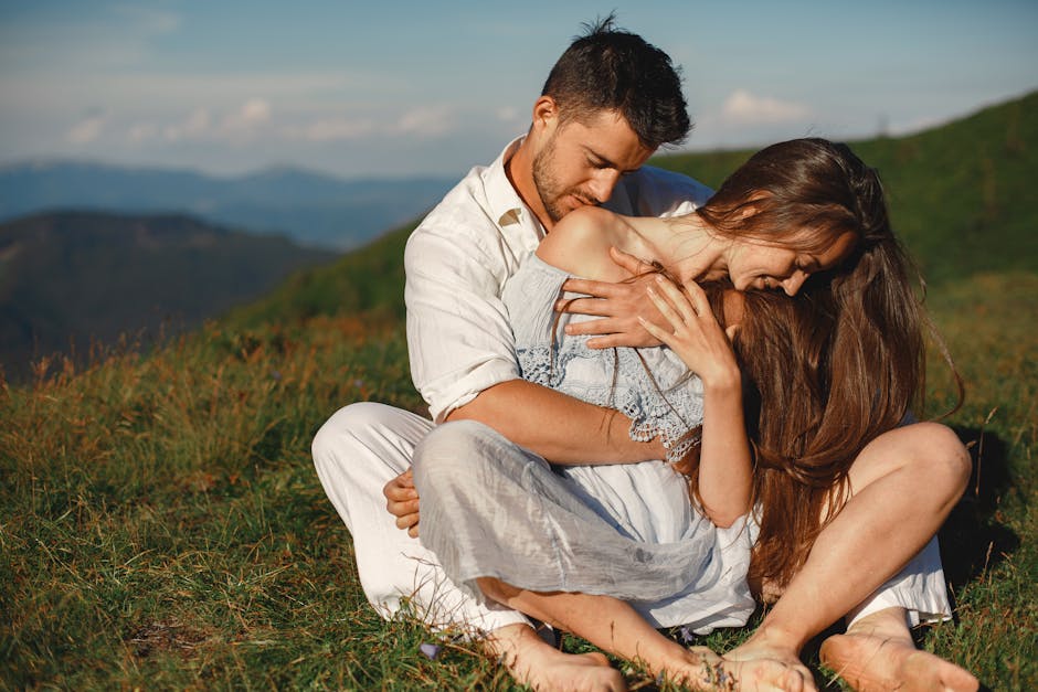Young couple embracing on a grassy hilltop, enjoying a romantic summer day.