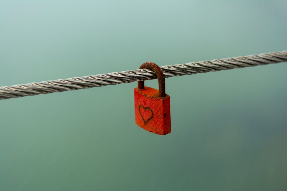 A rusty padlock with a heart hanging on a wire, symbolizing love or security.
