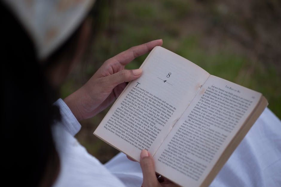 Person reading a book outdoors, enjoying a moment of tranquility and knowledge.