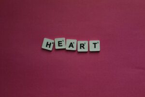Scrabble letter tiles spelling heart on a pink background for creative projects.