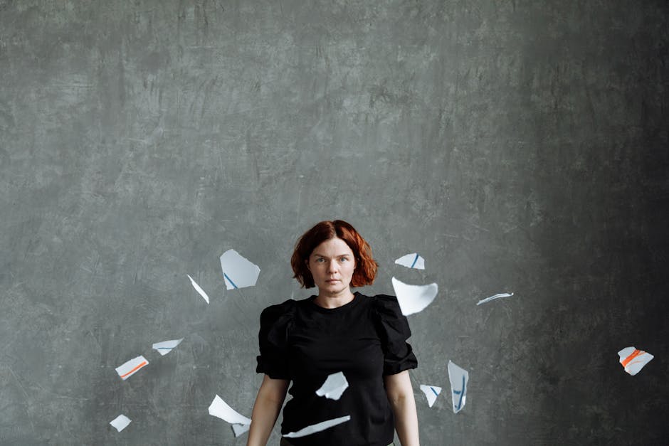 Portrait of a woman surrounded by scattered paper pieces on a gray backdrop.