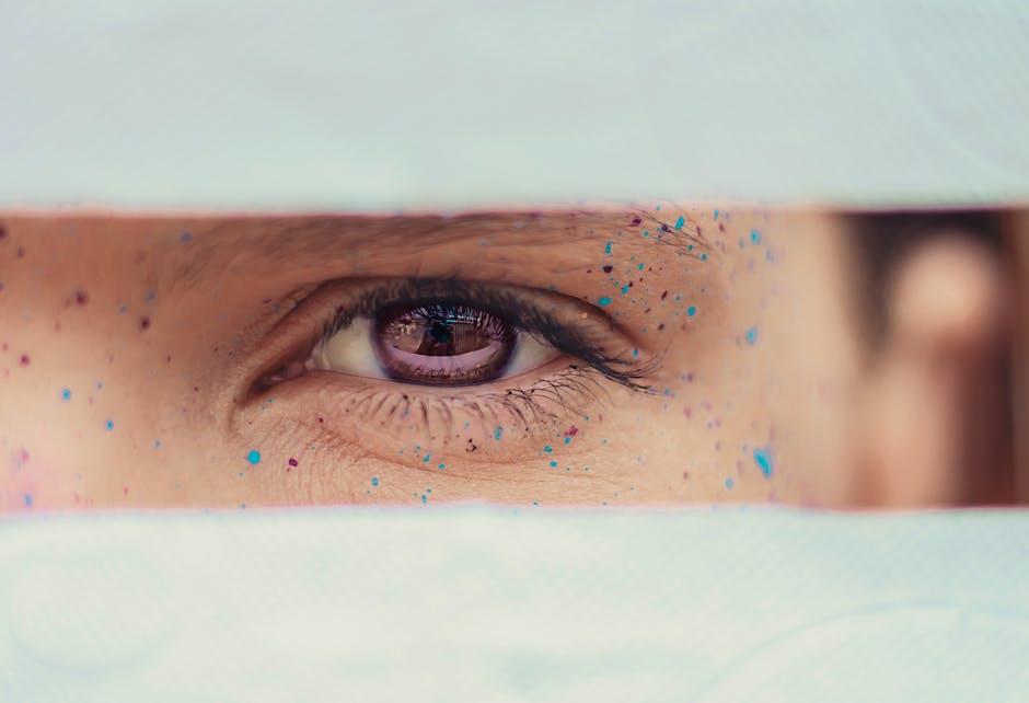 Selective focus crop calm female brown eye with multicolored paint spots on face skin looking at camera