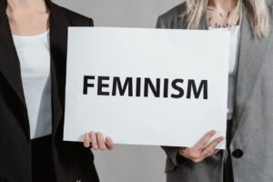 Two women in business attire holding a sign promoting feminism, emphasizing empowerment and equality.