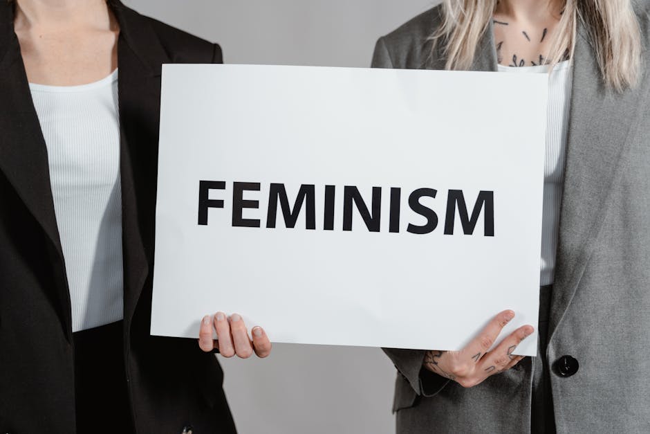 Two women in business attire holding a sign promoting feminism, emphasizing empowerment and equality.