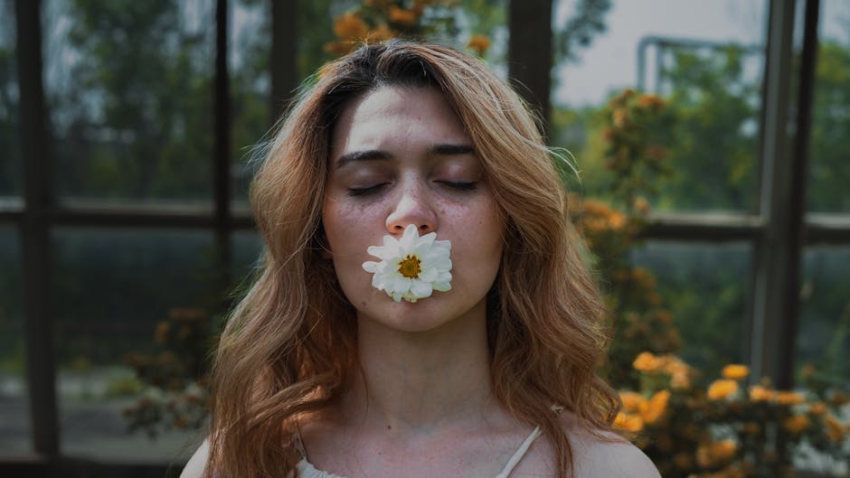 A woman with closed eyes holds a white flower in her mouth, surrounded by lush greenery.