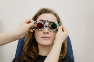 Unrecognizable female doctor correcting ophthalmic glasses selecting lenses on eyes of female patient during appointment in c