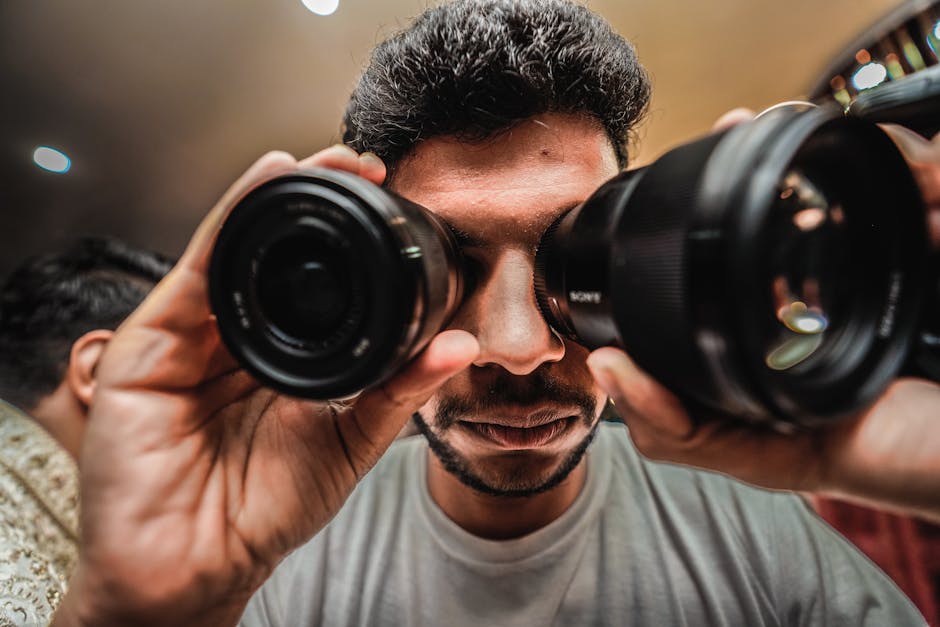 A creative portrait of a man using camera lenses as makeshift binoculars.