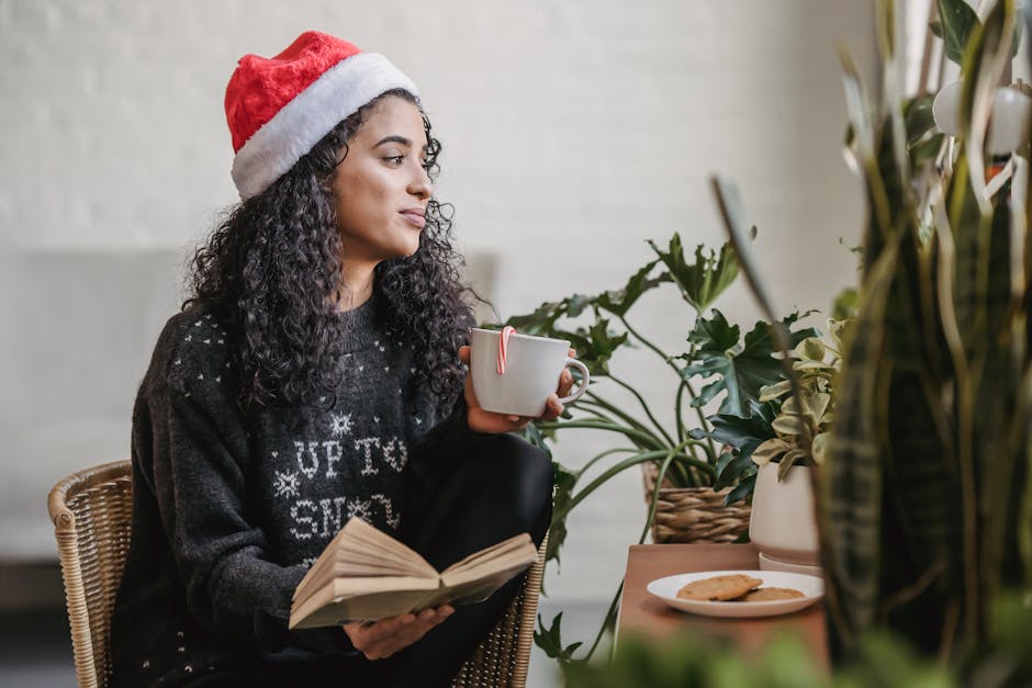 Concentrated young ethnic woman in Santa hat drinking hot chocolate and reading in cafe