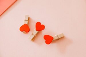 Close-up of three heart-shaped wooden clothespins on a soft pink background, perfect for Valentine's themes.