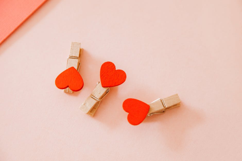 Close-up of three heart-shaped wooden clothespins on a soft pink background, perfect for Valentine's themes.