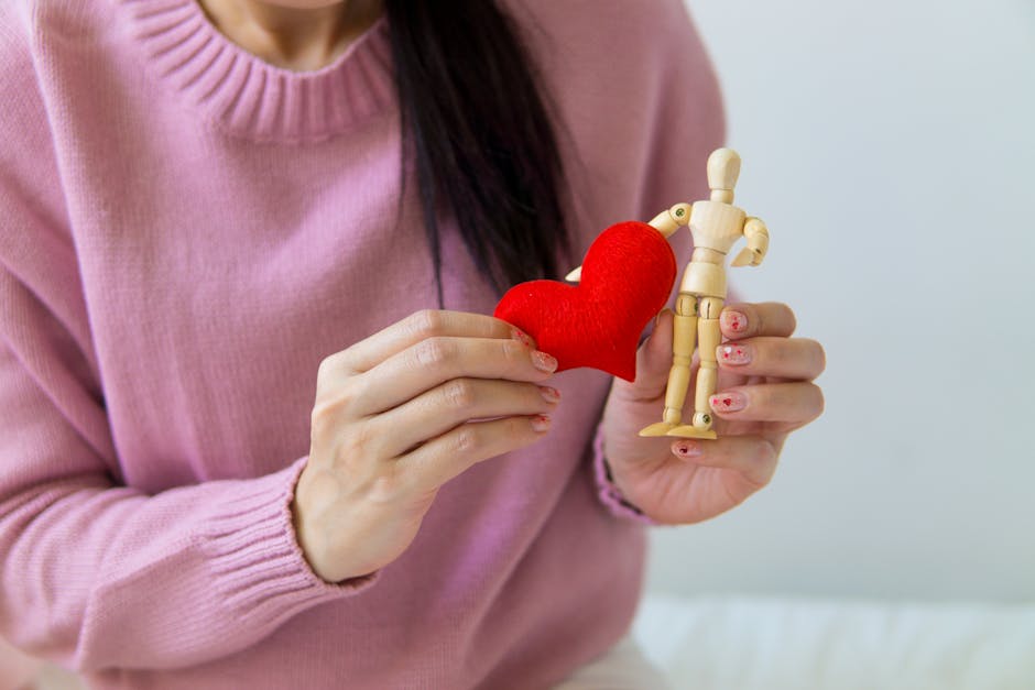Unrecognizable female with dark hair wearing pink sweater standing near white wall with small heart and wooden figure of man