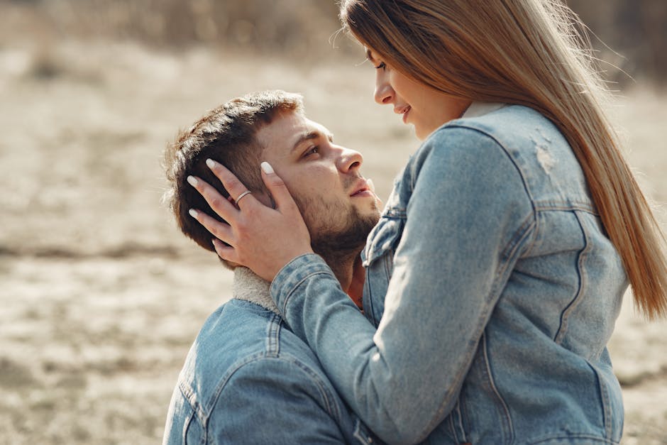 Side view of loving young couple in denim jackets hugging and looking at each other while spending time together on grassy me