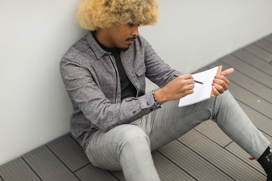 African American man deeply focused, writing thoughts in a notebook, sitting outdoors.