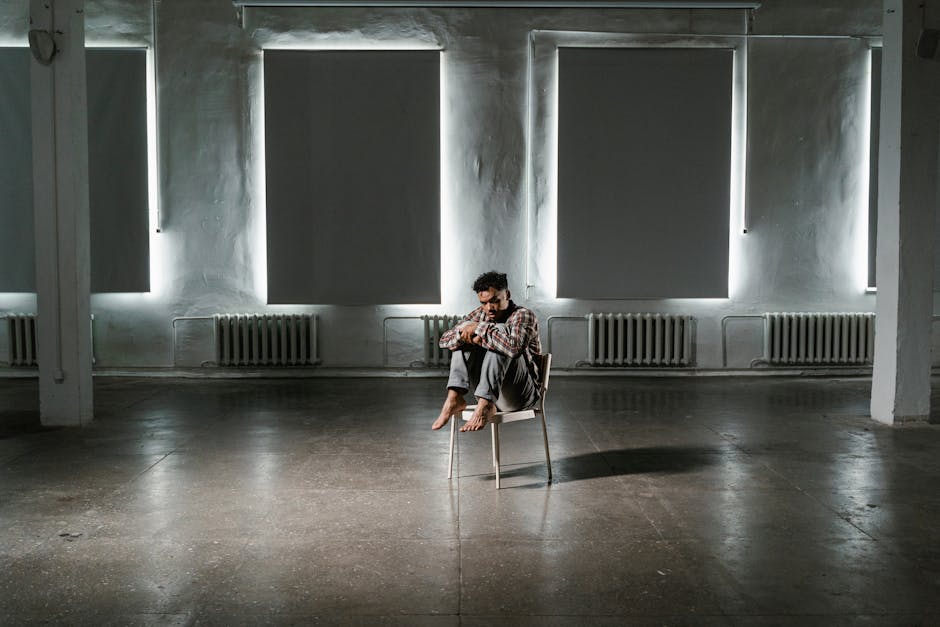 A contemplative man sits alone in an empty, minimalist room, creating a moody atmosphere.