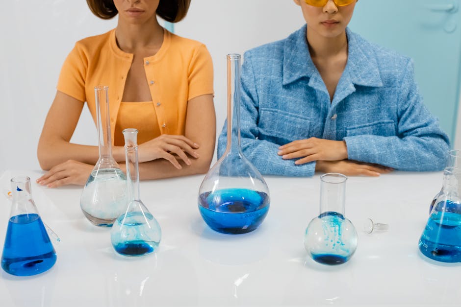Two women scientists in a lab with flasks conducting an experiment using blue liquid.