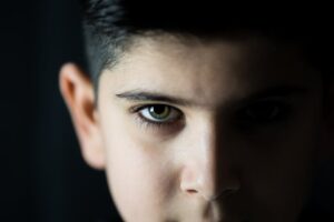 A close-up portrait of a child with green eyes in low light, capturing a pensive expression.