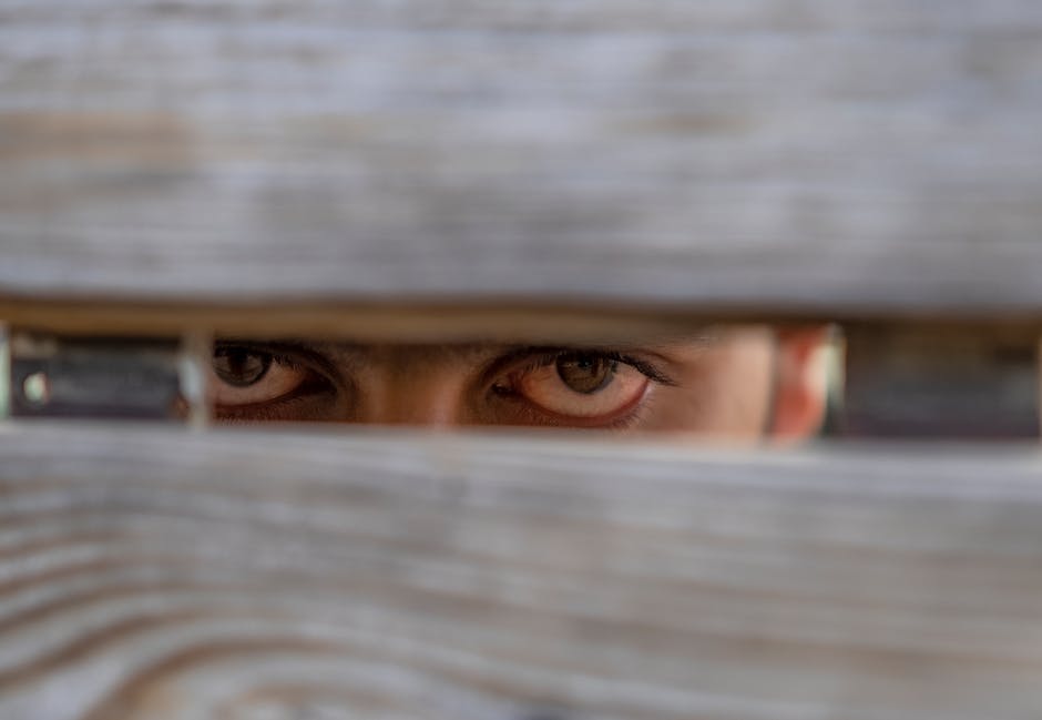 Mysterious eyes peering through a wooden fence. Concept of curiosity and hidden observation.