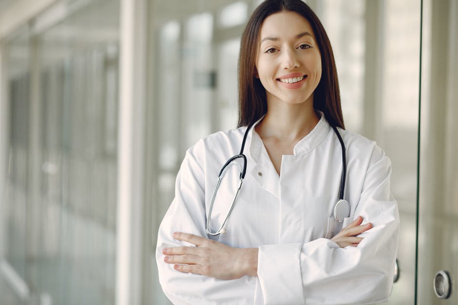 Crop cheerful ethnic female doctor in medical uniform and stethoscope holding hands crossed standing in modern clinic corrido