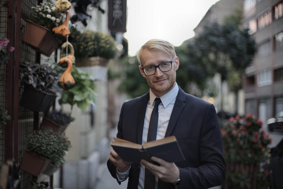 Confident male manager in glasses holding book and looking at camera while standing near plant store on sidewalk in city