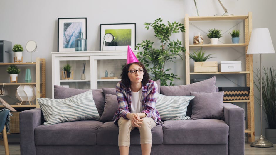 Thoughtful young woman with a party hat sitting on a sofa in a cozy living room.