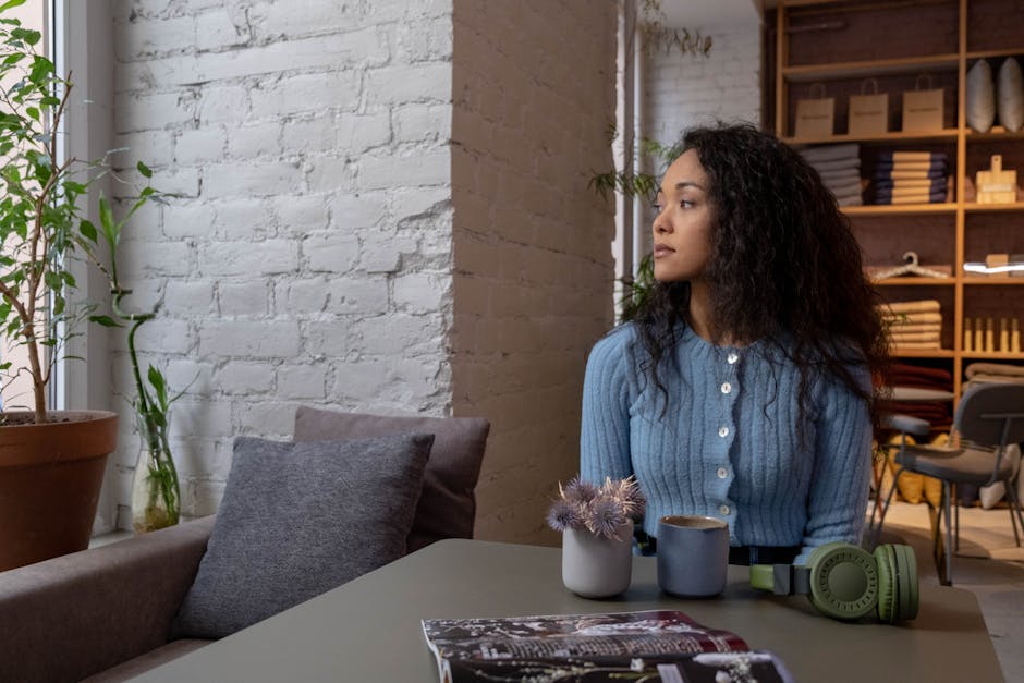 Young woman in a blue sweater enjoying a peaceful moment in a cozy cafe setting with a drink.