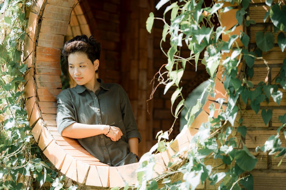 A young adult stands in a brick archway adorned with leafy vines, sunlit and serene.