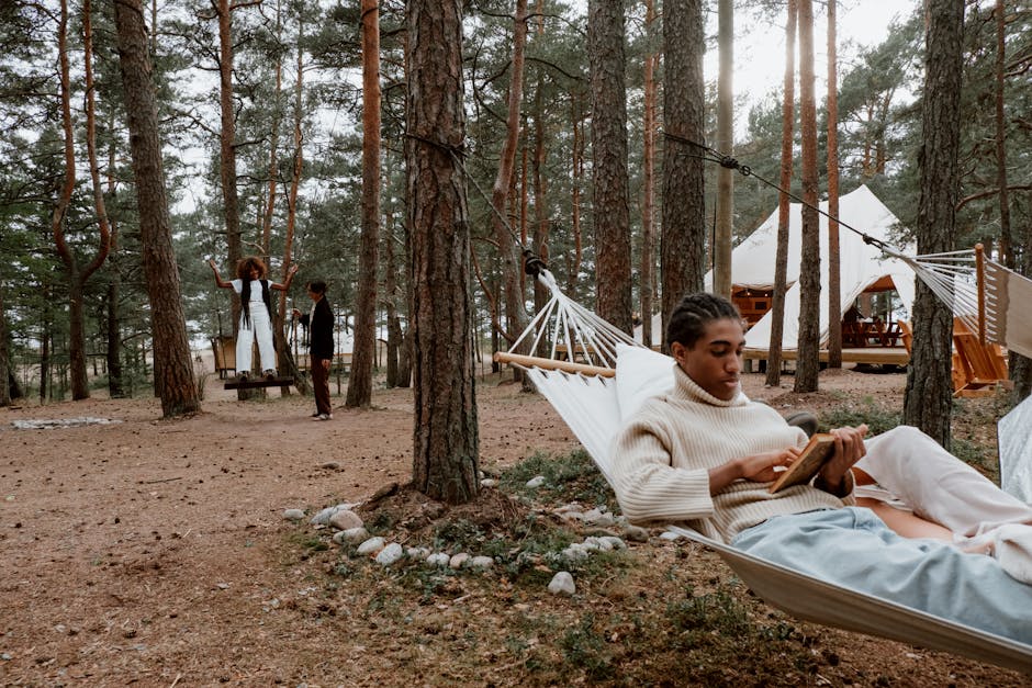 A man relaxes in a hammock reading a book in a tranquil forest setting.