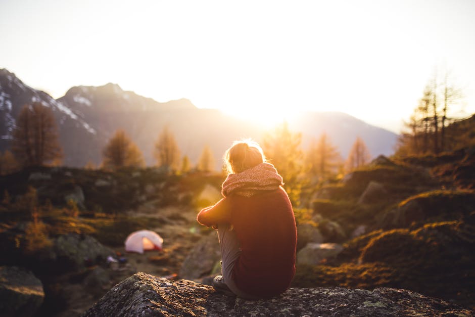 A woman sits on a rock enjoying the serene mountain view at sunrise in Sachseln, Switzerland.