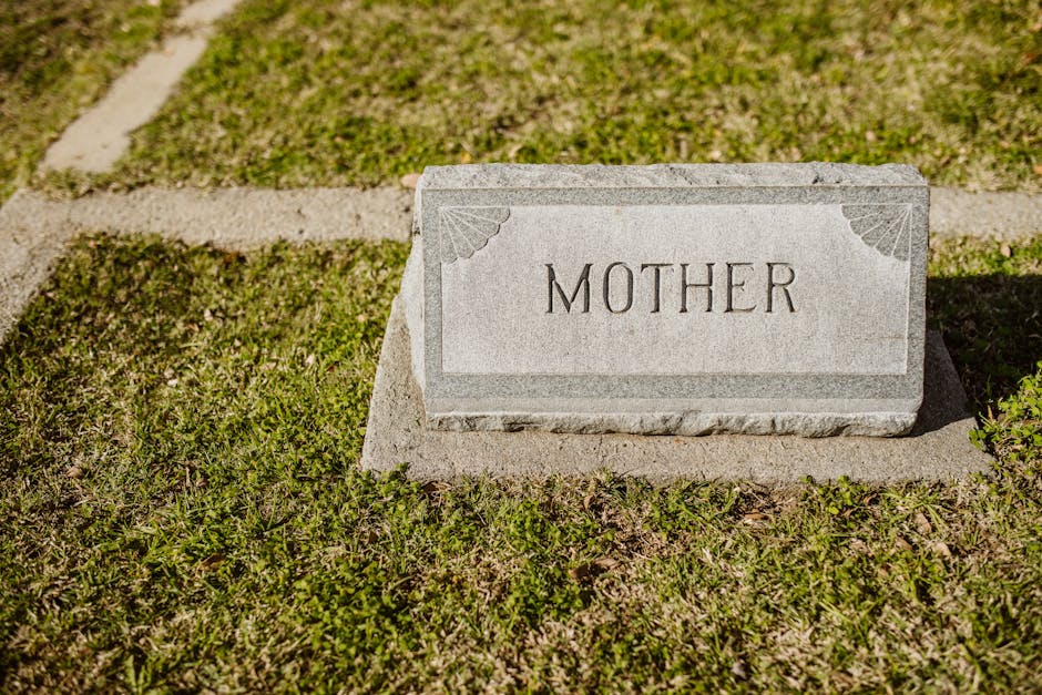 Gravestone in cemetery engraved with the word 'Mother' on grass.
