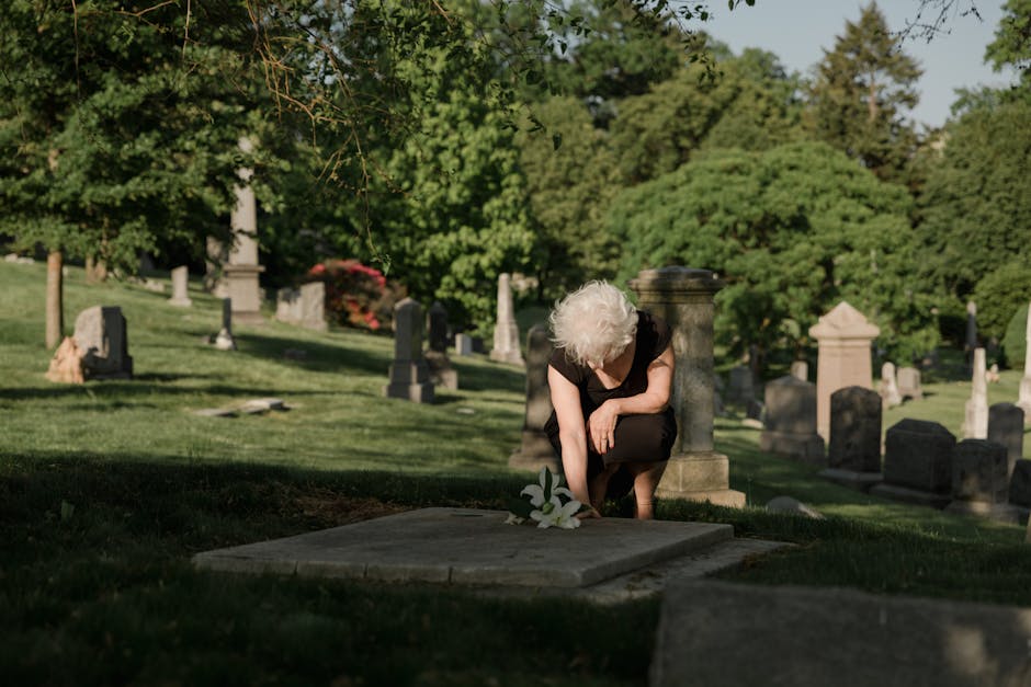 Senior woman placing flowers on a grave, symbolizing remembrance and grief.
