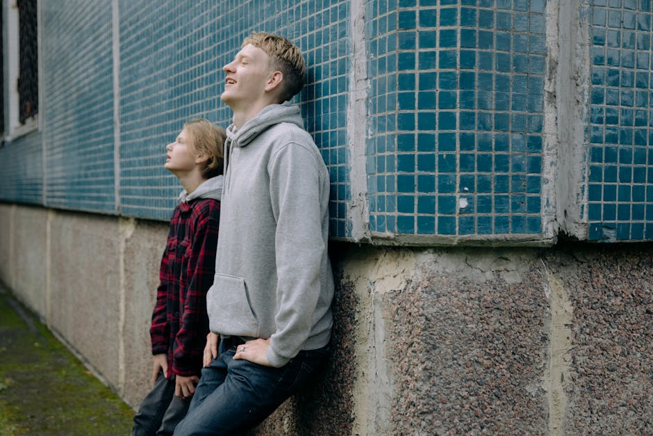 Two brothers bonding while leaning against a textured wall, enjoying the outdoors.