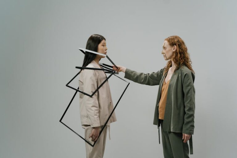 Young female model in green costume and beige top putting empty photo frames on shoulders of other female model wearing light