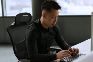 Asian man concentrated on typing at an office desk, in a formal setting.
