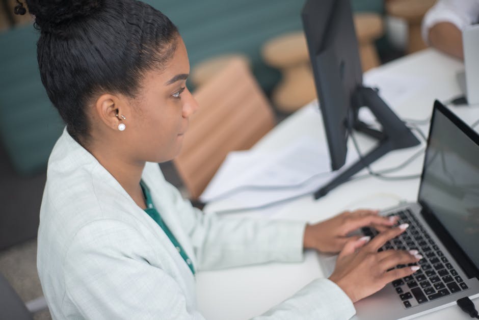 Young woman working diligently on her laptop in a modern office setting.
