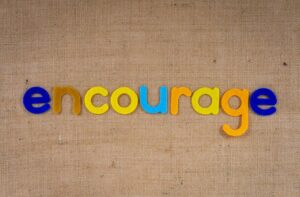 The word 'encourage' in colorful letters on a brown burlap texture, conveying positivity and motivation.