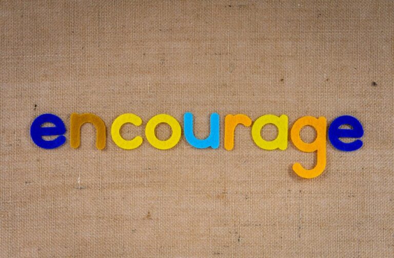 The word 'encourage' in colorful letters on a brown burlap texture, conveying positivity and motivation.