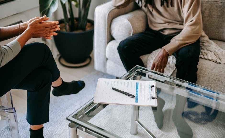 Crop anonymous African American man in casual clothes sitting on sofa and talking to female psychologist during psychotherapy