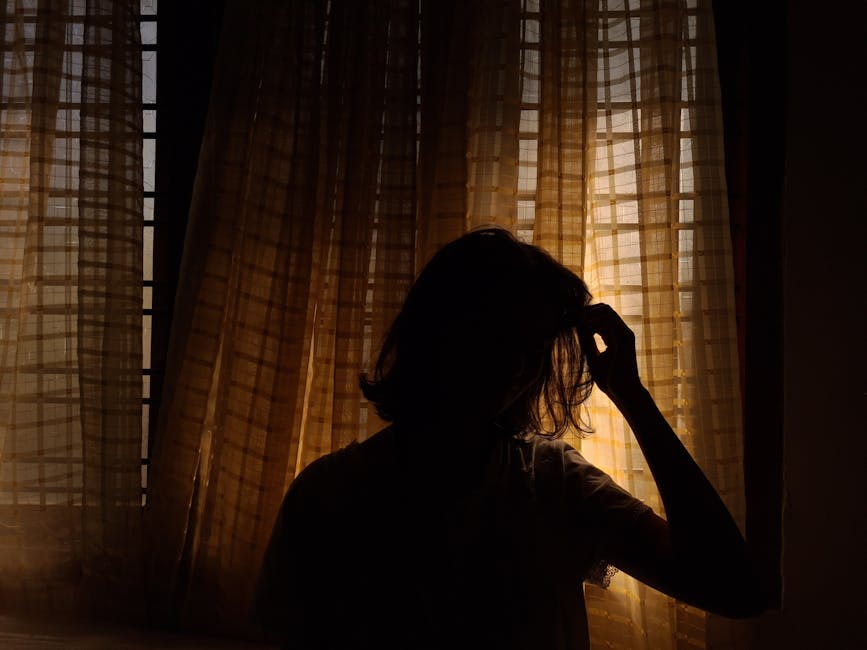 A dramatic silhouette of a woman standing by window curtains, highlighting texture and light.