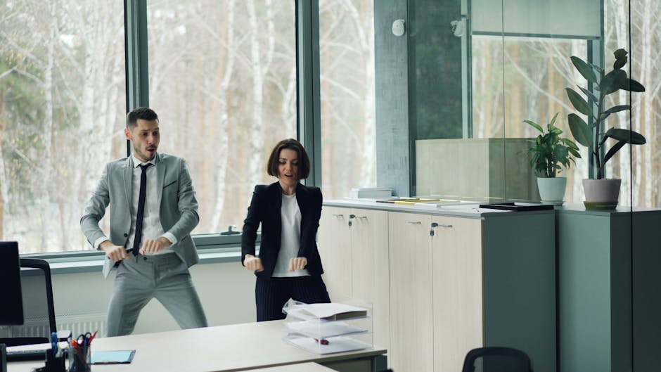 Two adults dance in a modern office space with large windows.