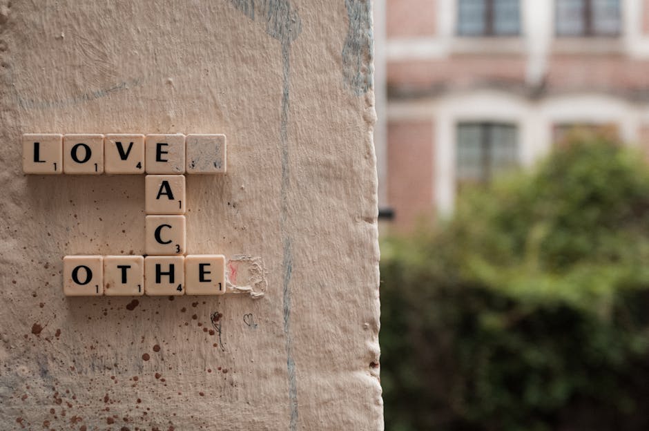 Scrabble tiles spelling 'Love Each Other' on a textured wall in Lille, France.