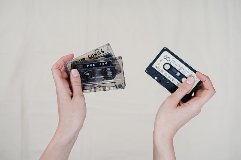 Two hands holding retro cassette tapes with handwritten labels, nostalgic music format.