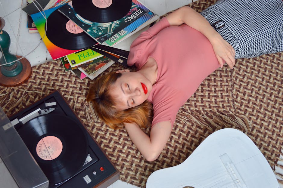 From above dreamy young female in casual wear lying on floor with eyes closed and hand behind head while listening to vinyl r